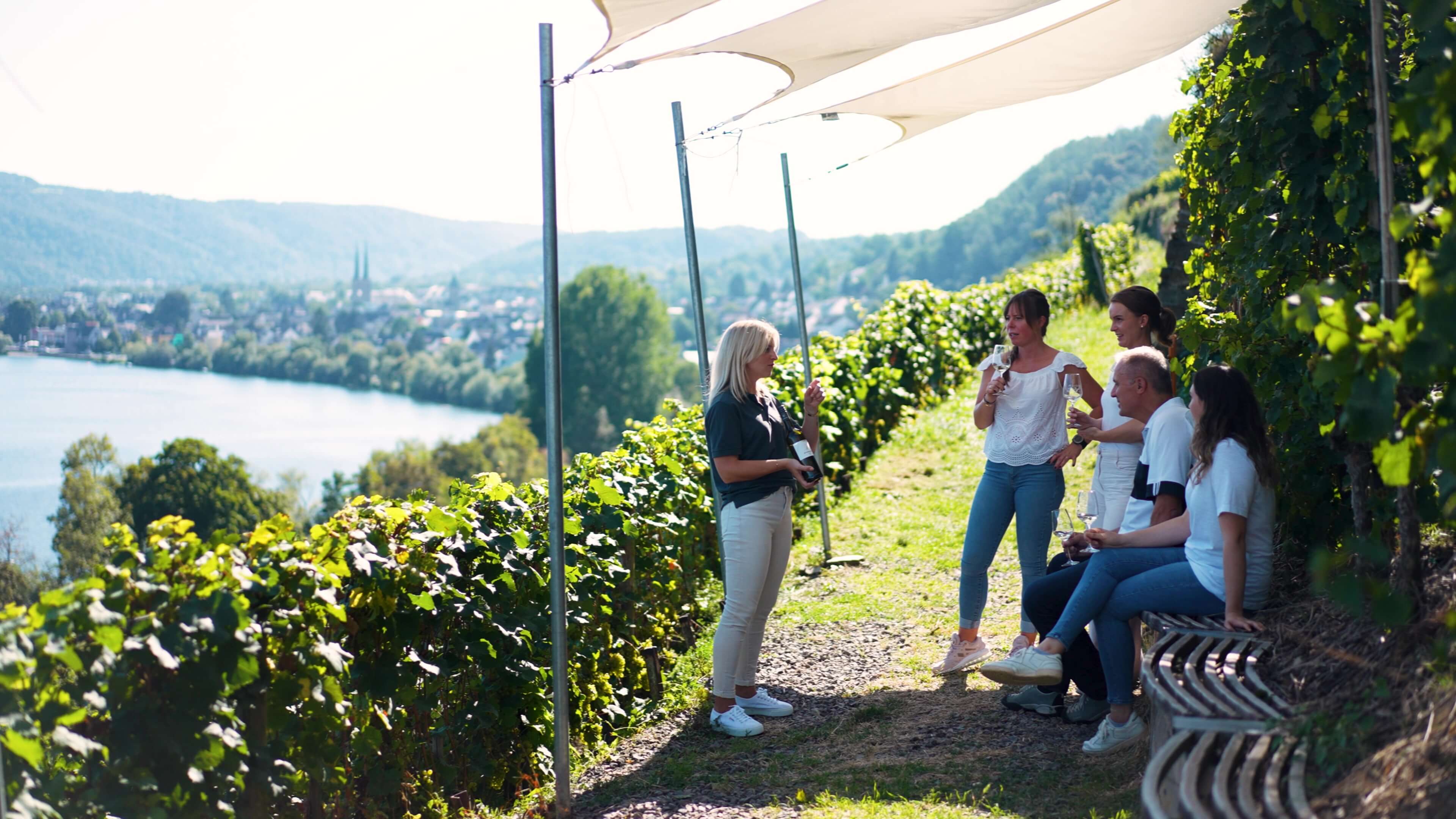 Tourguide erklärt Wein während der Amreinbergtour an Gäste mit Blick auf den Weinberg und Mosel im Koblenzer Marienberg vom Weingut Schwaab